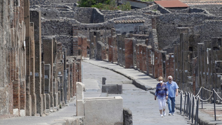 A man and a woman walk among the ruins of Pompeii