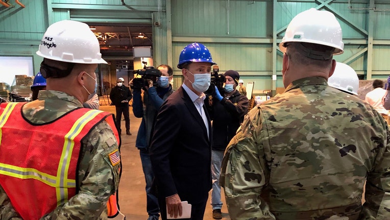 Gov. Ned Lamont wears a hard hat and mask with members of the media and National Guard
