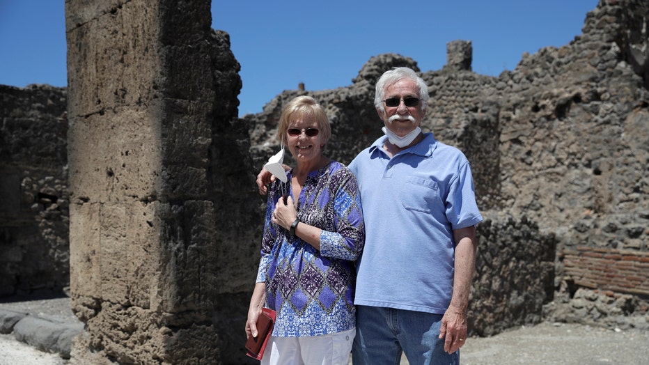 A woman and a man stand among the ruins of Pompeii