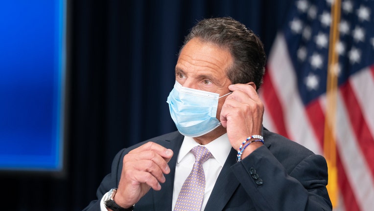 Gov. Andrew Cuomo wears a blue mask, American flag is behind him