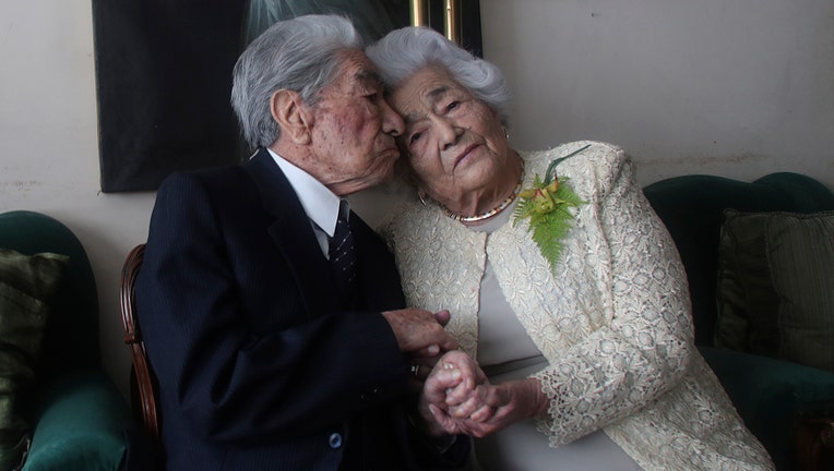 A man and woman, a married couple, sit on a couch with their heads lightly touching