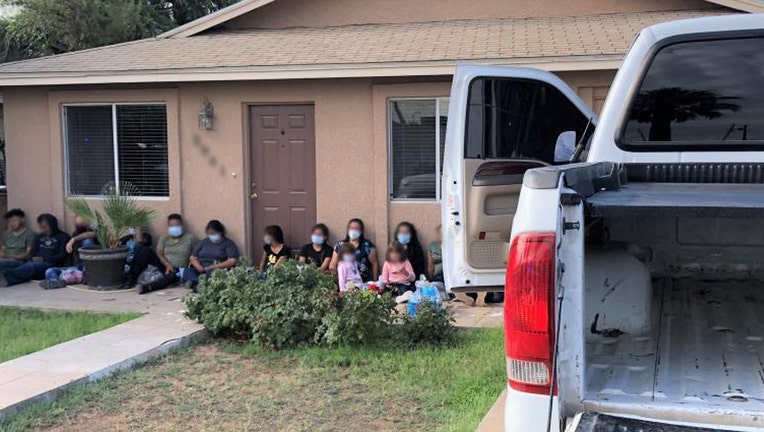 Migrants with their faces blurred sitting against a house