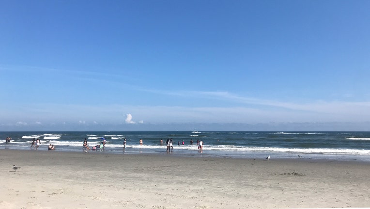 A blue sky over a stretch of beach with waves breaking in Atlantic City; about a dozen people are in and out of the water