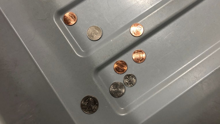 A quarter, a dime, two nickels, and four pennies left behind in a gray plastic bin at an airport checkpoint
