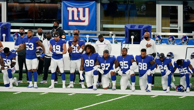 Giants football players in blue and white uniforms; some stand, some kneel on the field