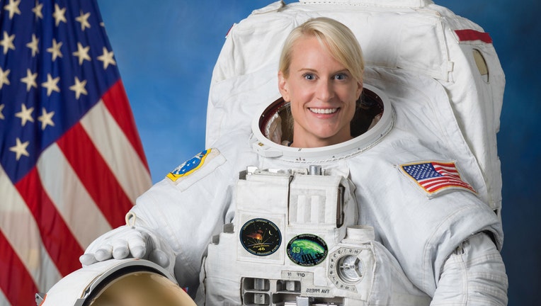 A smiling astronaut in a white space suit with American flag behind her