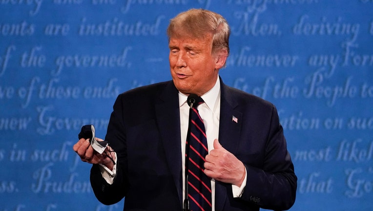Trump holds a face mask in his right hand as he stands on the debate stage in front of a blue backdrop