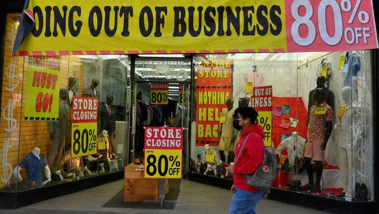 A person wearing a face mask walks past a store going out of business