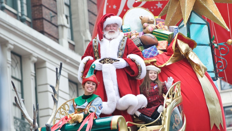 Santa Claus, an elf, and a little girl on a sleigh at the Macy's Thanksgiving Day Parade
