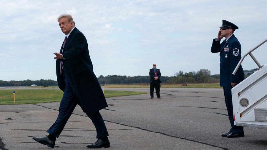 Trump, wearing an overcoat, walks away across tarmac as an Air Force master sergeant salutes