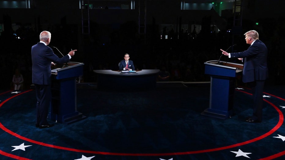 Biden and Trump seen from behind stand at lecterns on a stage facing moderator Chris Wallace sitting at a desk