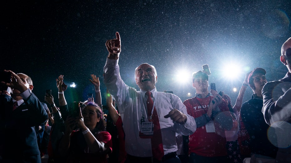 Several people wave and cheer at a nighttime campaign rally