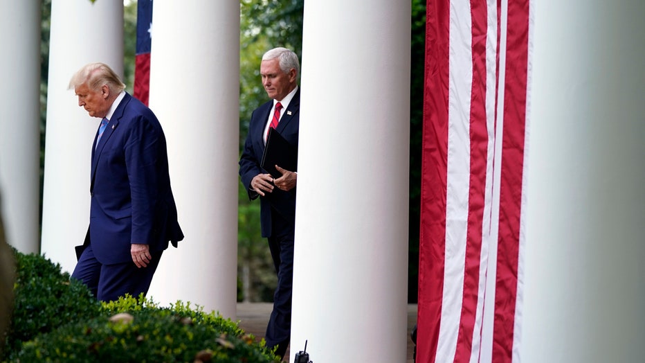 Trump and Pence walk in between some columns and bushes at the White House