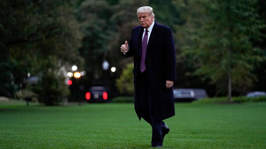 Trump, wearing an overcoat and a purple tie, makes a thumb's up gesture as he walks across the White House lawn