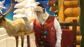 Santas don face shields, stand behind plexiglass to meet children