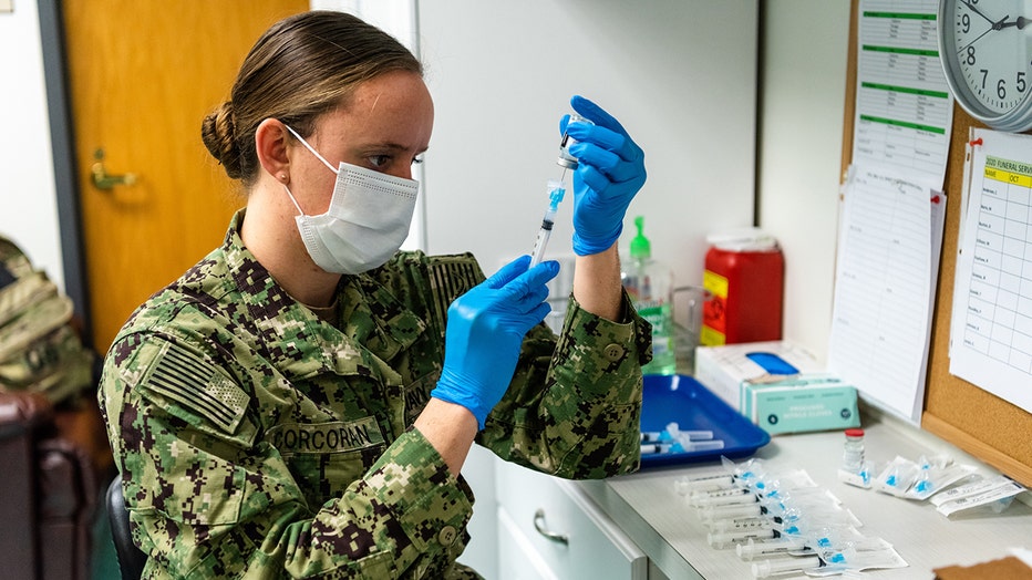 Navy medic in camo and a mask prepares a syringe