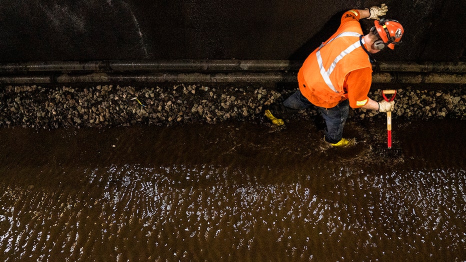 View from above of a worker in orange safty gear testing a flooded rail bed in a tunnel