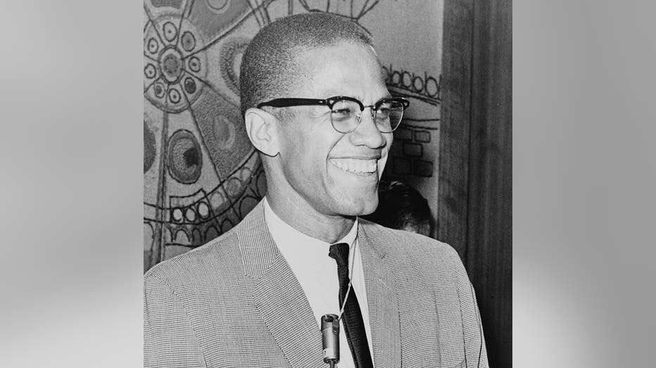 Smiling Malcolm X, half-length portrait, facing right, wearing glasses, suit, tie and small microphone