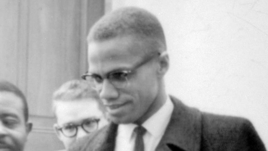 head and shoulders view of a smiling Malcolm X wearing glasses, coat and tie