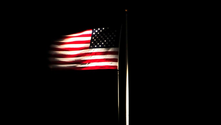 An illuminated American flag waves at night