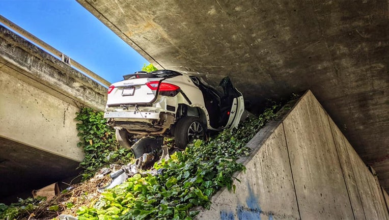 This photo provided by the California Highway Patrol shows the scene where a man fleeing from the CHP totaled his girlfriend's Maserati SUV after he careened up an embankment and slammed into the underside of an overpass, wedging the car under a freeway in Oakland, Calif., on Monday, April 12, 2021. (California Highway Patrol