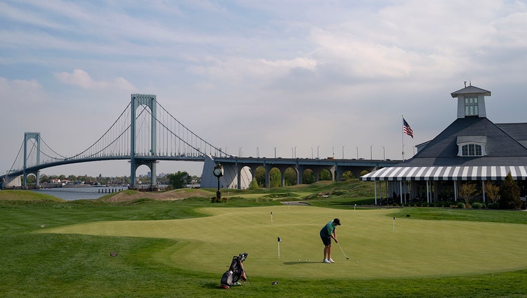 Patrons practice on the putting green beside the clubhouse as the Whitestone Bridge looms in the distance at Trump Golf Links at Ferry Point in the Bronx