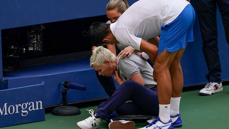 Tennis player leans over to check on a line umpire who sits on the court holding her throat