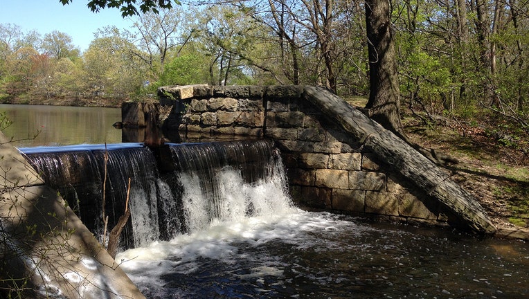 A spillway from Hempstead Lake; the sides of the spillway have stone walls; many trees are around