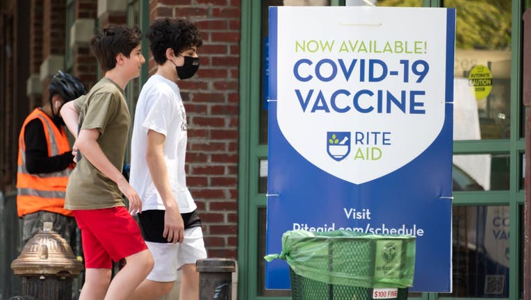 People walk by a sign that reads, "Now available! COVID-19 vaccine" in TriBeCa