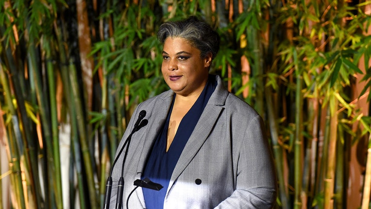 Author Roxane Gay wearing a gray and blue outfit speaks into a microphone; behind here are large bamboo trees