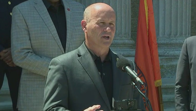 Police Commissioner Patrick Ryder wearing a gray suit speaks into a microphone outdoors