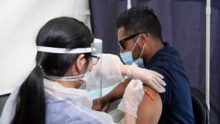 Medical worker in PPE gives a shot to a man wearing a light blue mask and a dark blue shirt