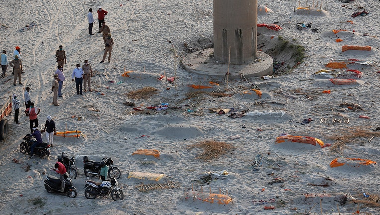 Policemen stand next to the bodies buried in shallow graves on the banks of Ganges river in Prayagraj, India, Saturday, May 15, 2021. Police are reaching out to villagers in northern India to investigate the recovery of bodies buried in shallow sand graves or washing up on the Ganges River banks, prompting speculation on social media that they were the remains of COVID-19 victims. (AP Photo/Rajesh Kumar Singh)