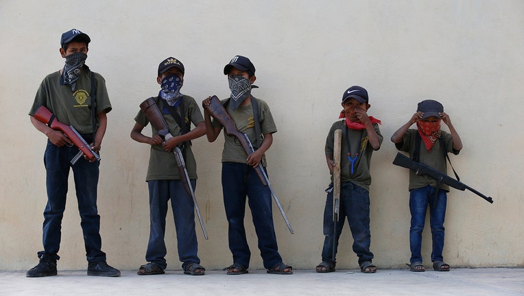 Children hold their training weapons, some real and some fake, during a display for the media designed to attract the federal government's attention to the dangers of organized crime their town negotiates daily in Ayahualtempa, Guerrero state, Mexico, Wednesday, April 28, 2021. International organizations have condemned the "recruitment" of children and warned of the effects. (AP Photo/Marco Ugarte)