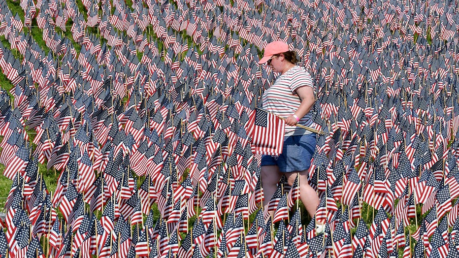A volunteer wearing a cap, shorts, and T-shirt carries American flags among a sea of flags at Boston Common