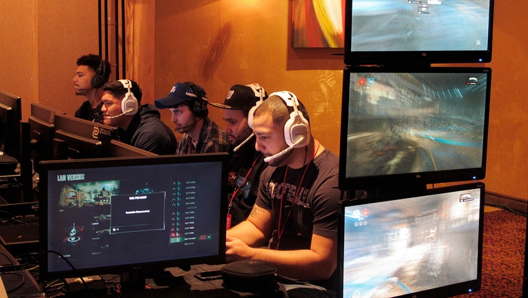 5 gamers wearing headsets sit next to each other as face monitors and play video games inside a casino