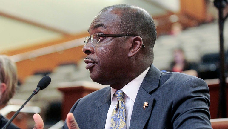Head and shoulders view of Mayor Brown wears glasses, suit, and paisley tie; he is speaking into a microphone