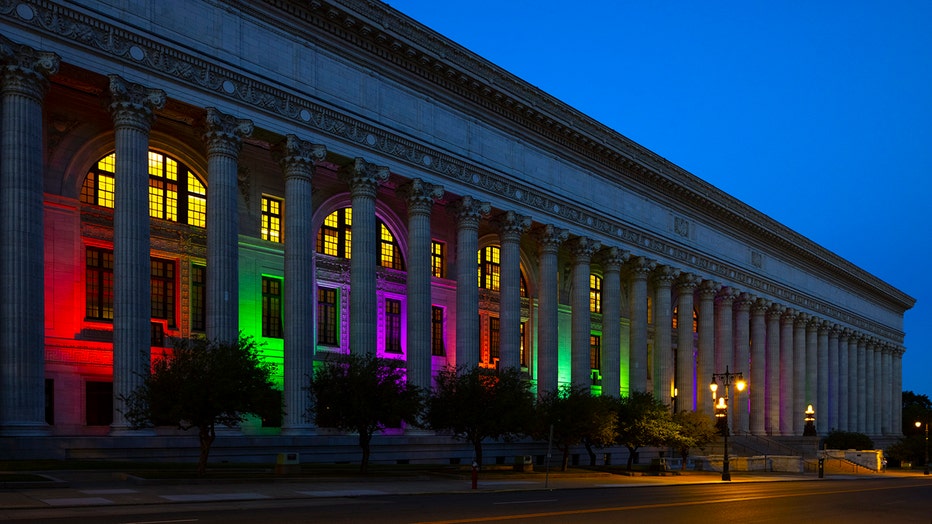 A long building woth columns illuminated for Pride