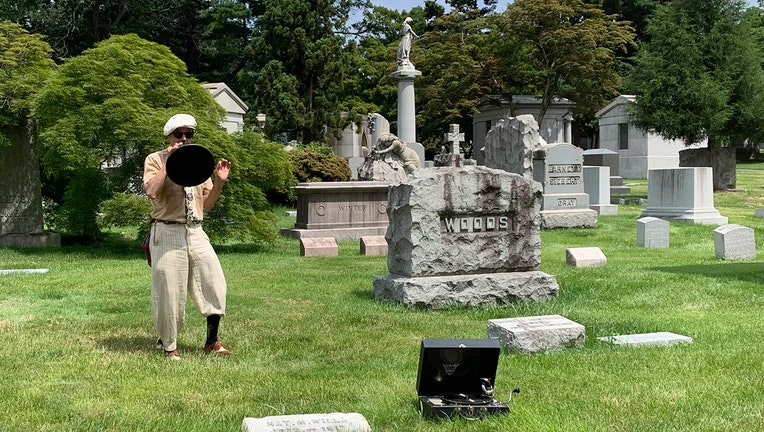 Tour guide wearing period clothes speaks into a vintage megaphone among some graves in a scenic cemetery