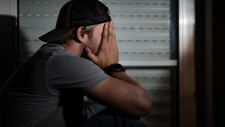 A man sits in his apartment and puts his hands in front of his face. 