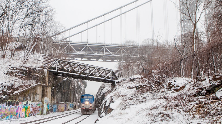 An Amtrak train seen passing under George Washington Bridge and an overpass on a snowy day