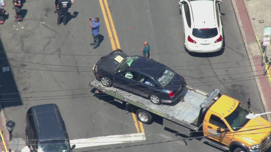 A damaged dark-colored sedan on a flatbed truck seen from the sky
