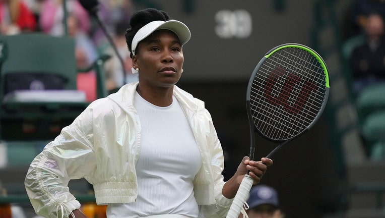 Venus Williams wears a white visor, white jacket and white shirt and holds a tennis racket