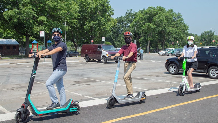 3 people wearing helmets and masks ride electric scooters