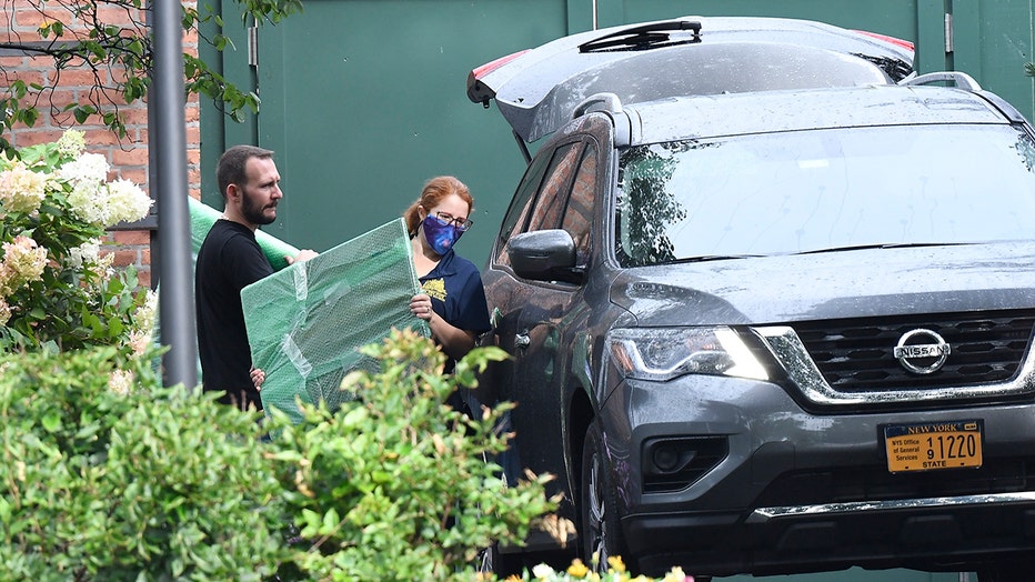Two people carry items packed in bubble wrap to a vehicle
