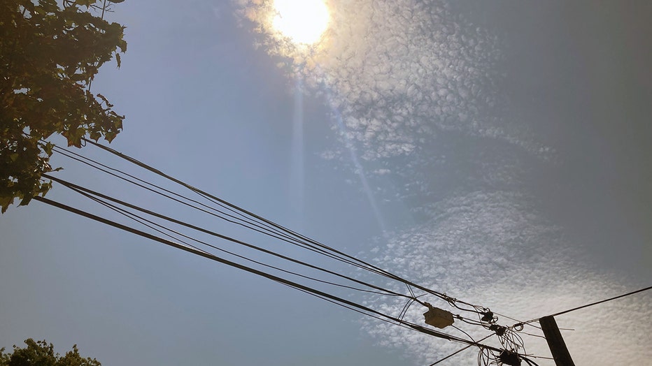 The white-hot sun in the hazy sky with trees on the left and power lines at the bottom