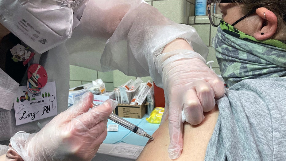 Nurse in gloves and mask gives a shot in arm of a woman wearing a green mask and glasses