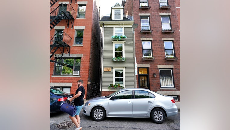 A man in blue shorts and carrying a bag walks by Boston's famous Skinny House, a 4-story wood frame with planters at each window