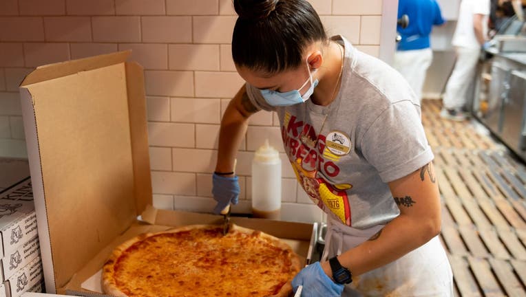 An employee wearing a protective face mask and gloves prepares pizza at King Umberto Restaurant. 