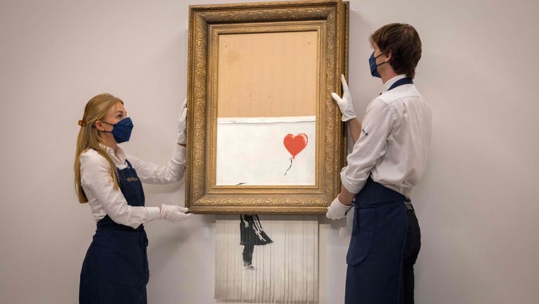 Assistants pose by an artwork titled Love is the Bin by British street artist Banksy during a photocall at Sothebys auction house in central London on September 3, 2021.
